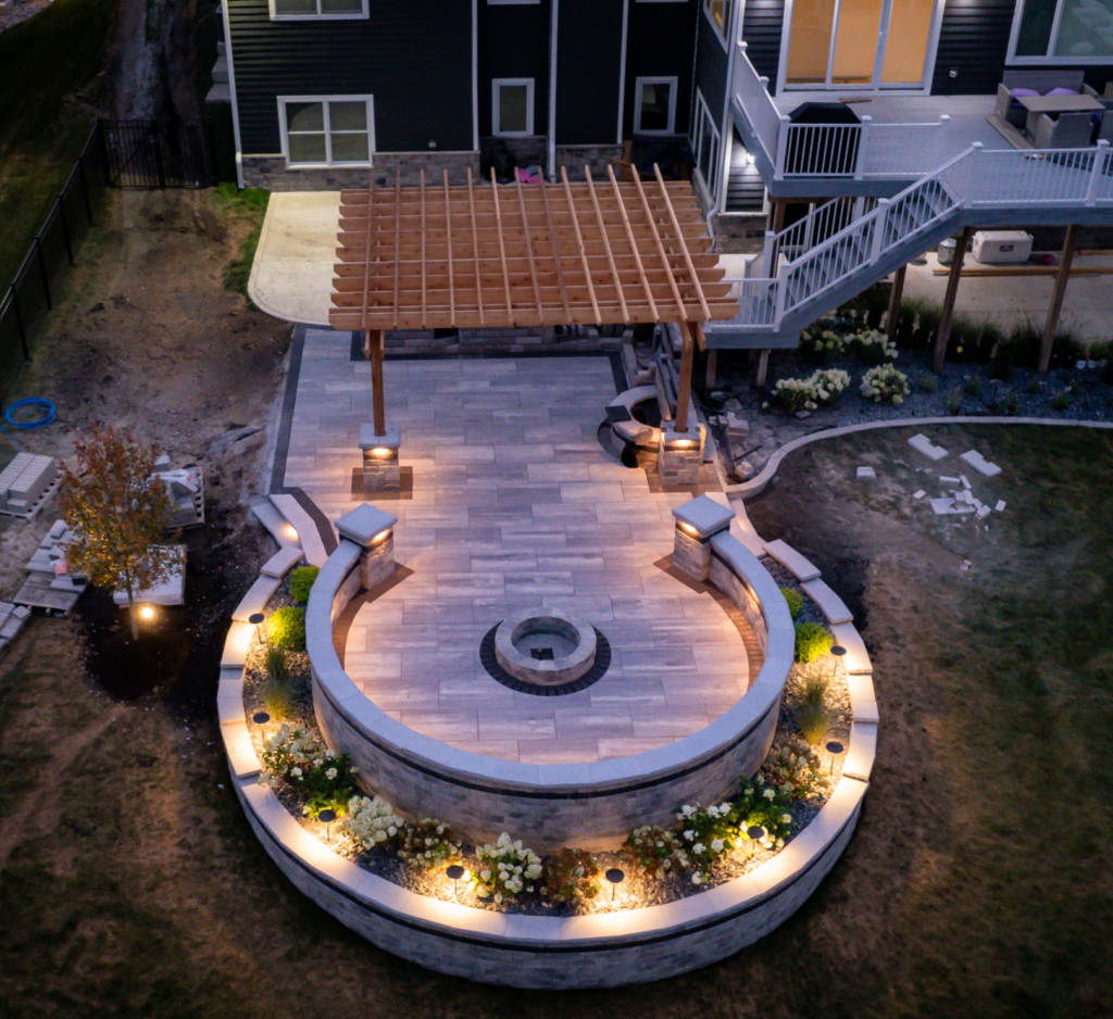 An aerial view of a patio with a fire pit and a pergola at night.