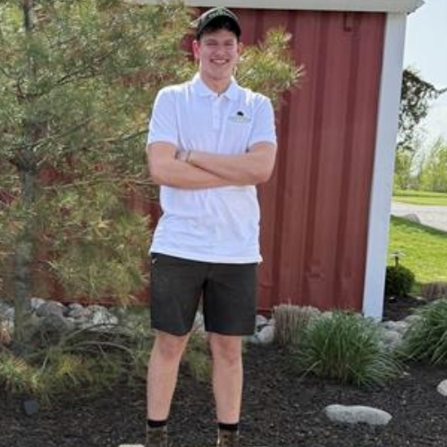 Jorge wearing sunglasses and a hat is standing in front of a red building.