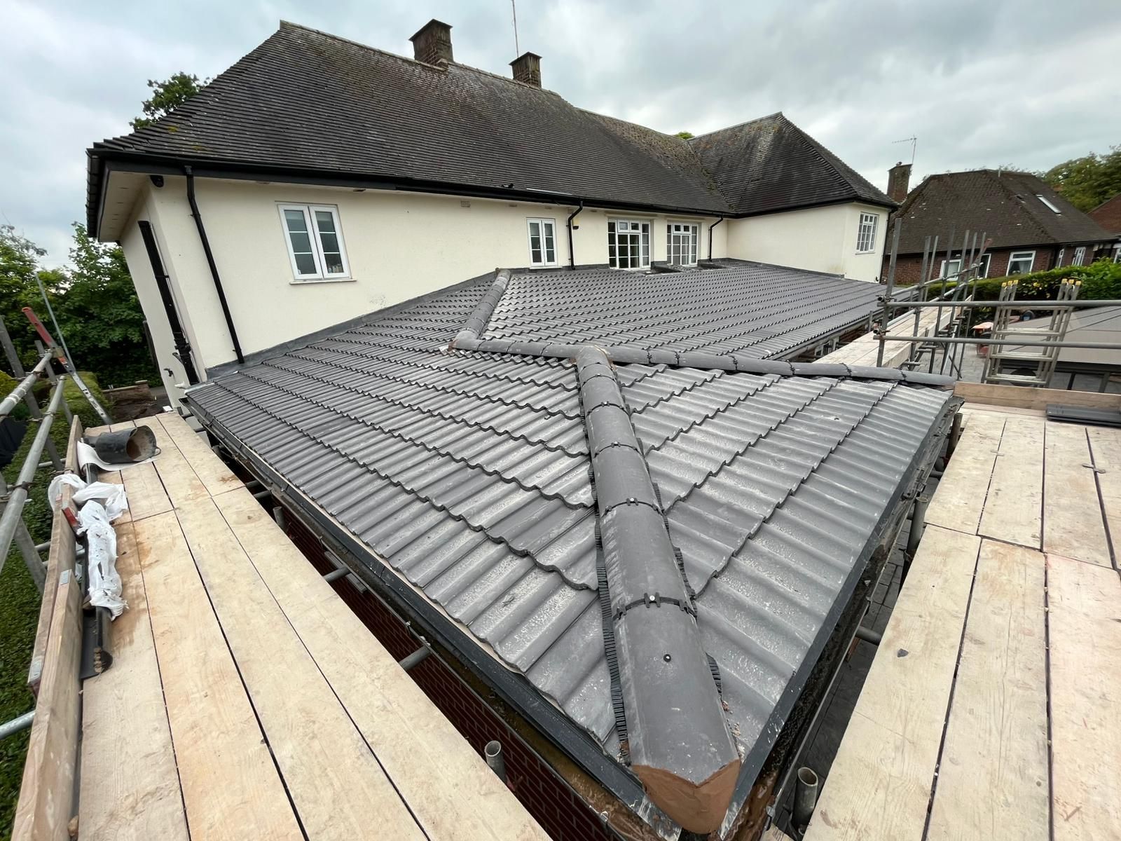 House with gray tile roof, construction scaffolding, cloudy sky.
