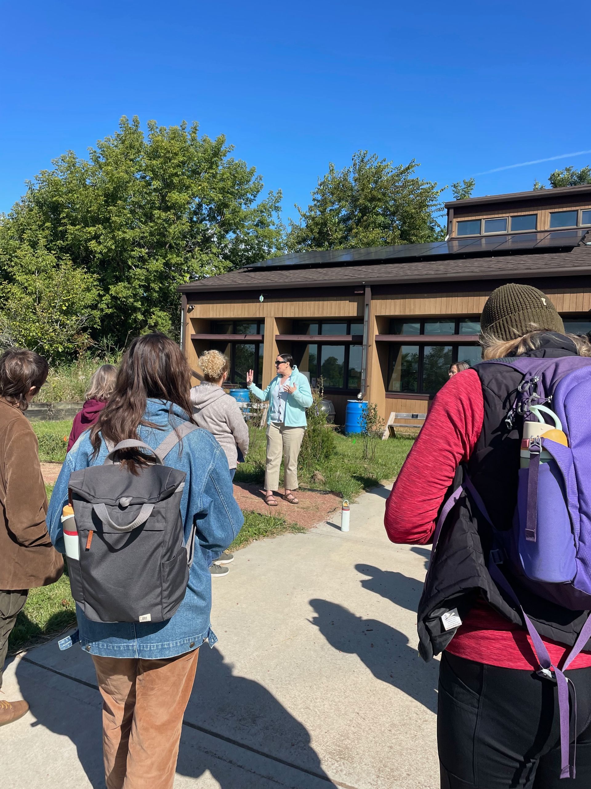 A group on a sunny day listens to a guide in front of a building with solar panels.