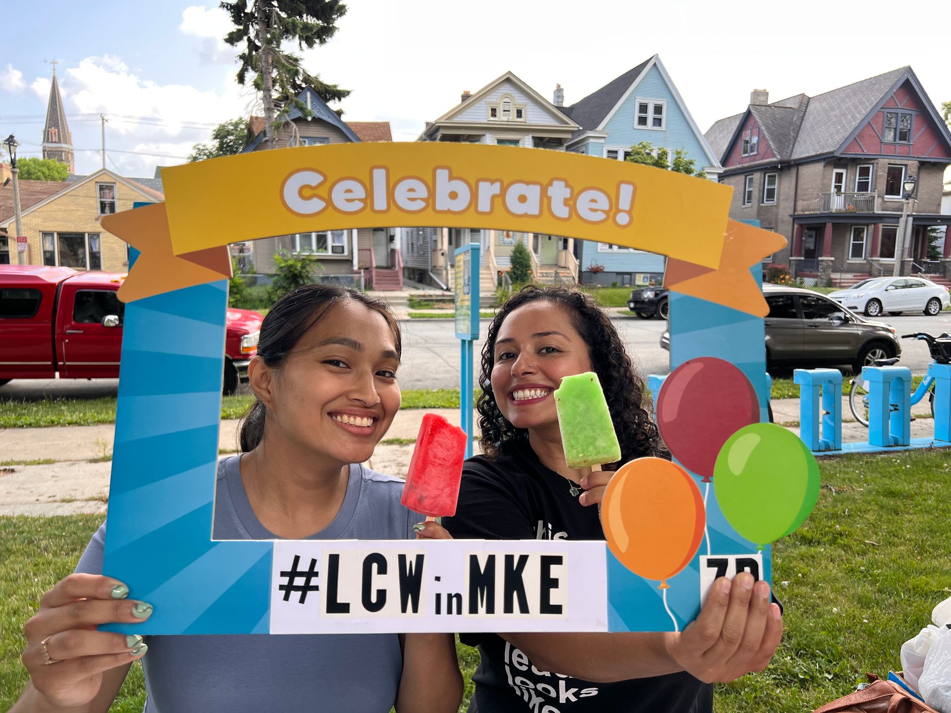 Two women eating popsicles and holding up a frame that reads 