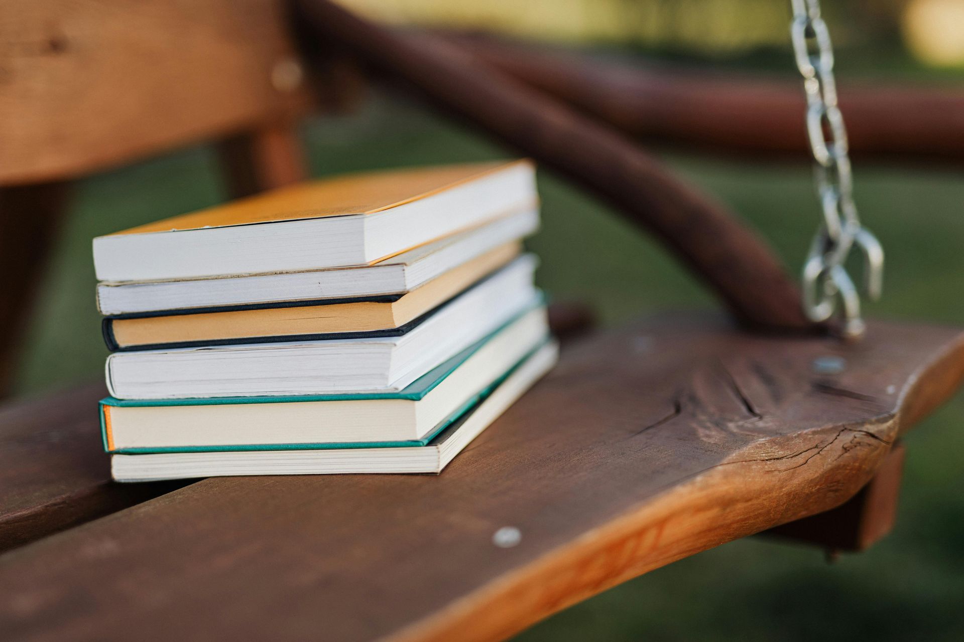 A small stack of five books resting on a wooden swing outdoors.