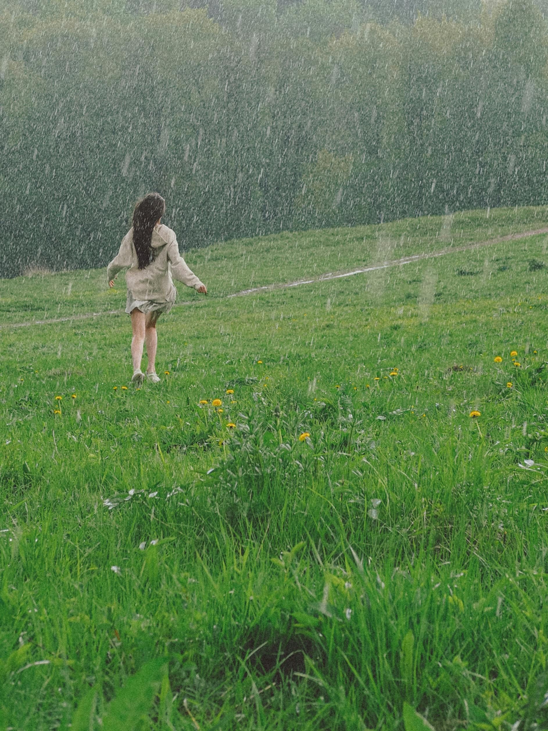 Person in a light dress walking through a green field in the rain.