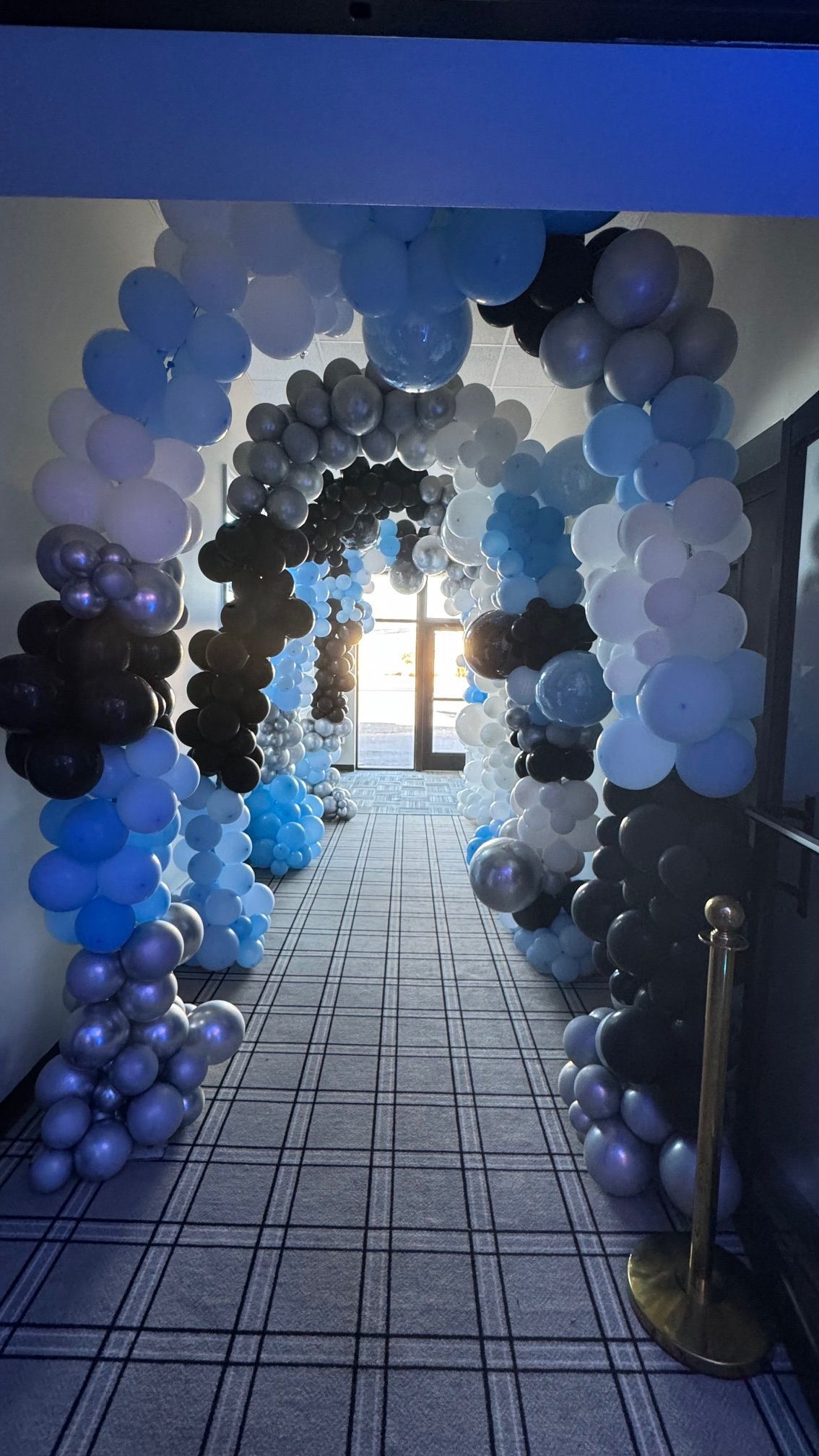 A hallway filled with blue , white , and black balloons.
