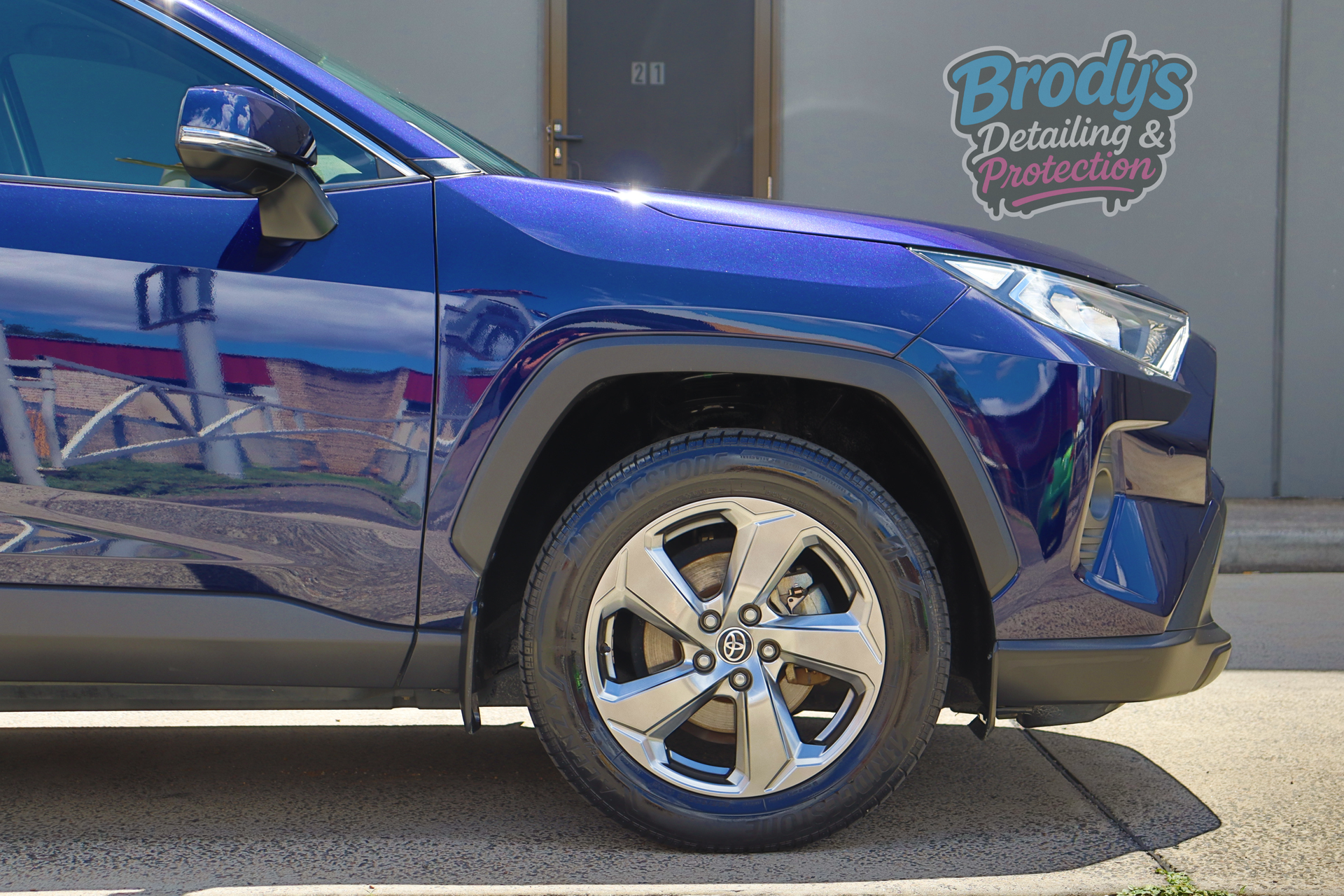 Blue Toyota SUV with shiny wheels parked in front of a building.