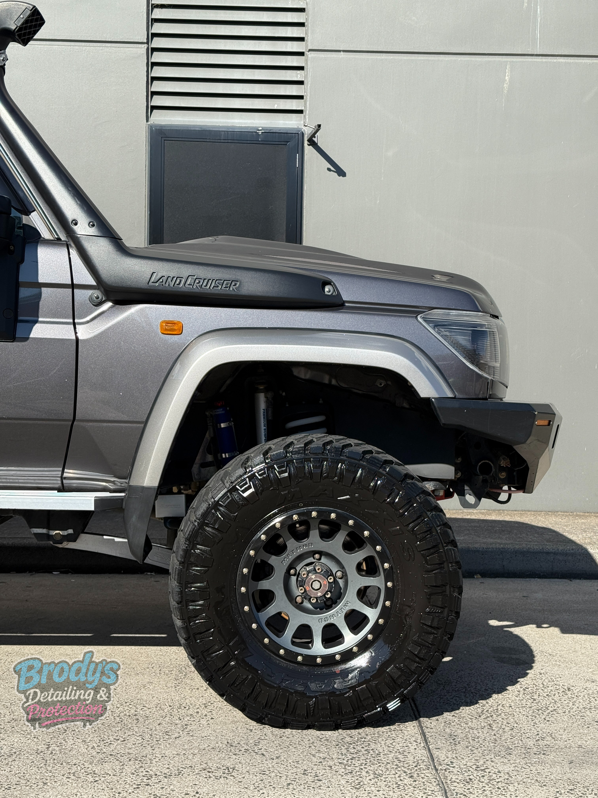 Grey off-road Toyota Land Cruiser with a snorkel, black wheels, and a rugged bumper parked near a building. — Brody’s Car Detailing In Tamworth, NSW