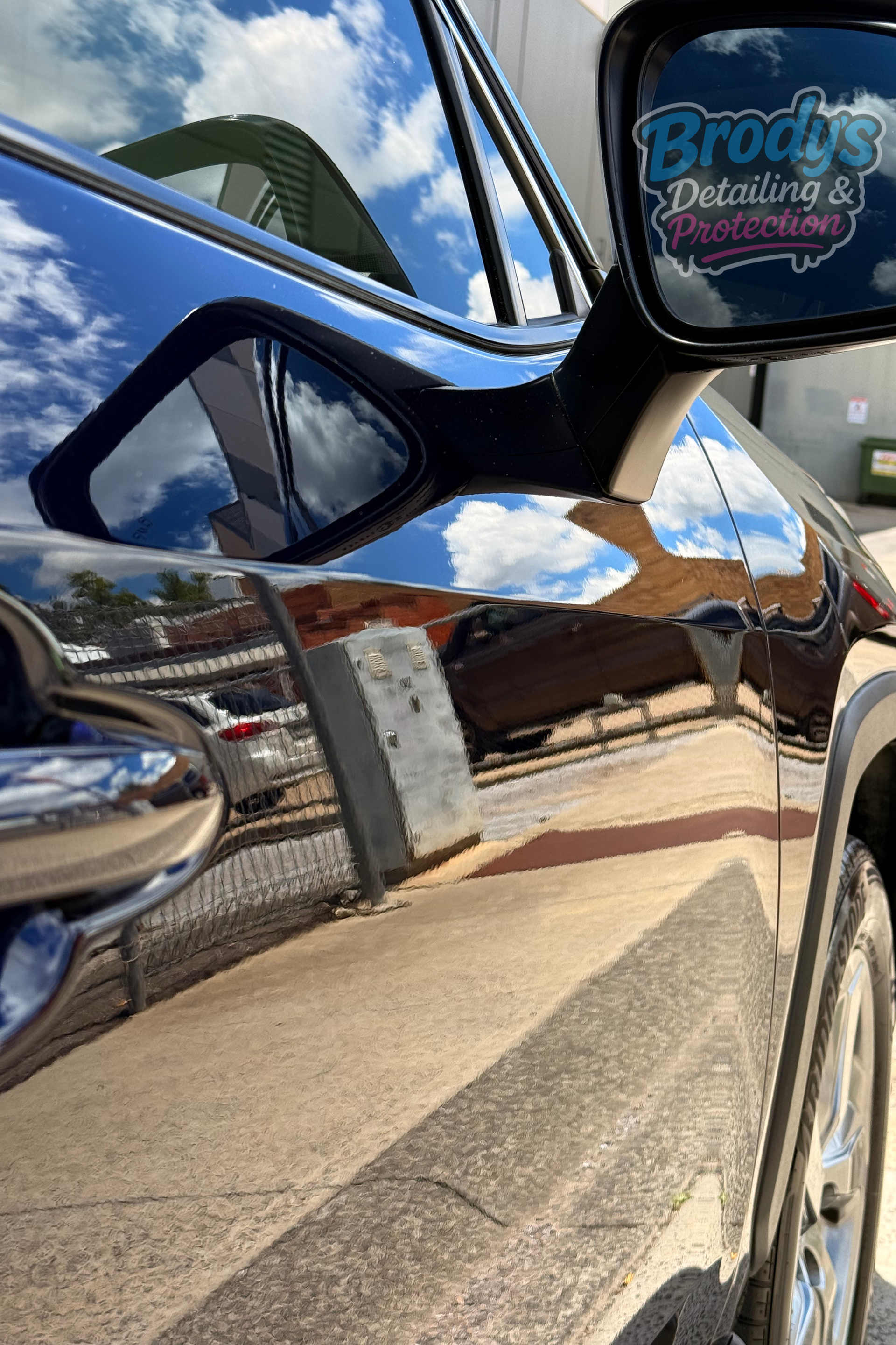 Black car with glossy paint reflecting sky and surroundings, including a side mirror with a detailing business logo. — Brody’s Car Detailing In Tamworth, NSW