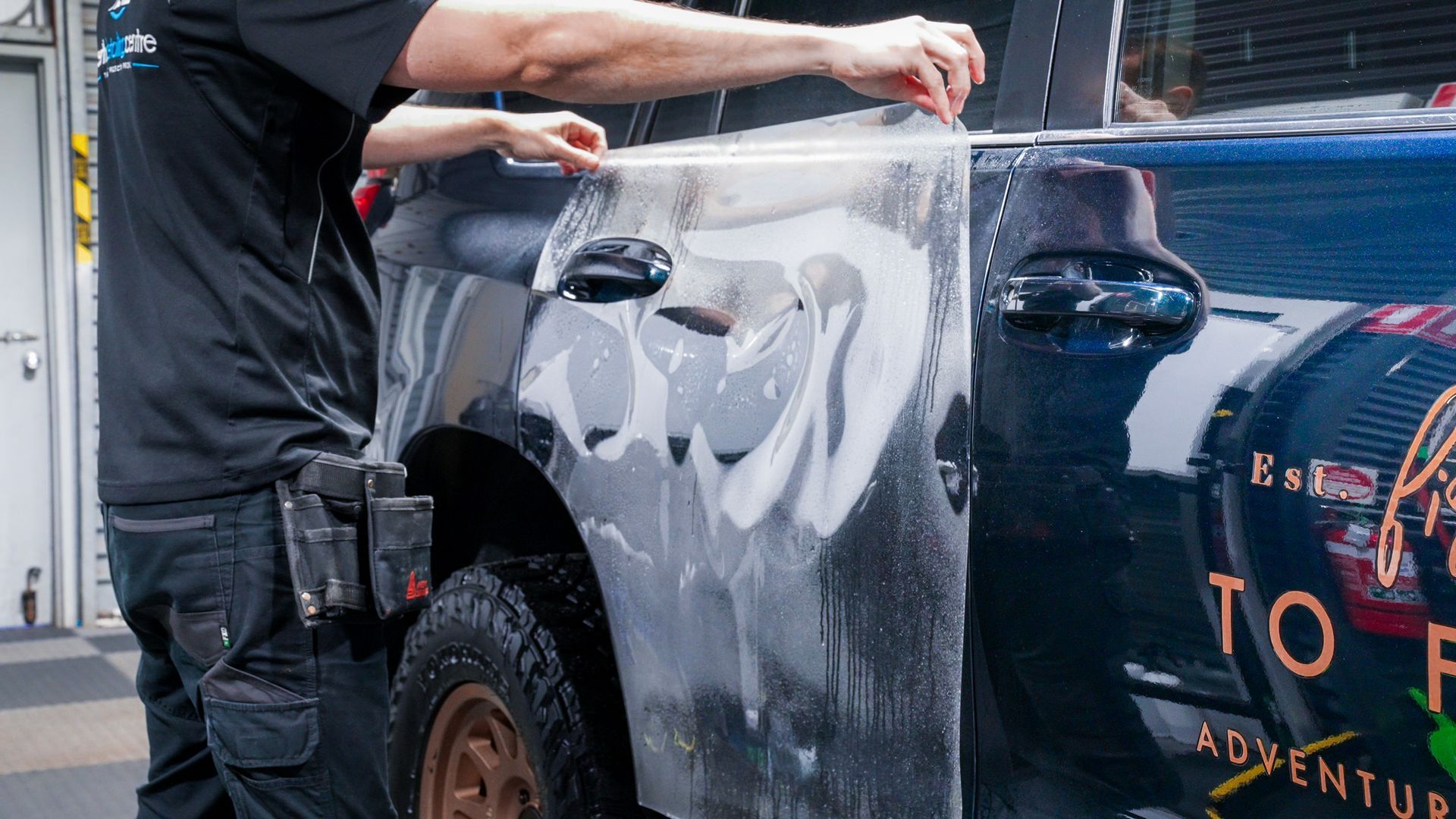 Man applying protective film to a dark blue car door in a shop. — Brody’s Car Detailing In Tamworth, NSW