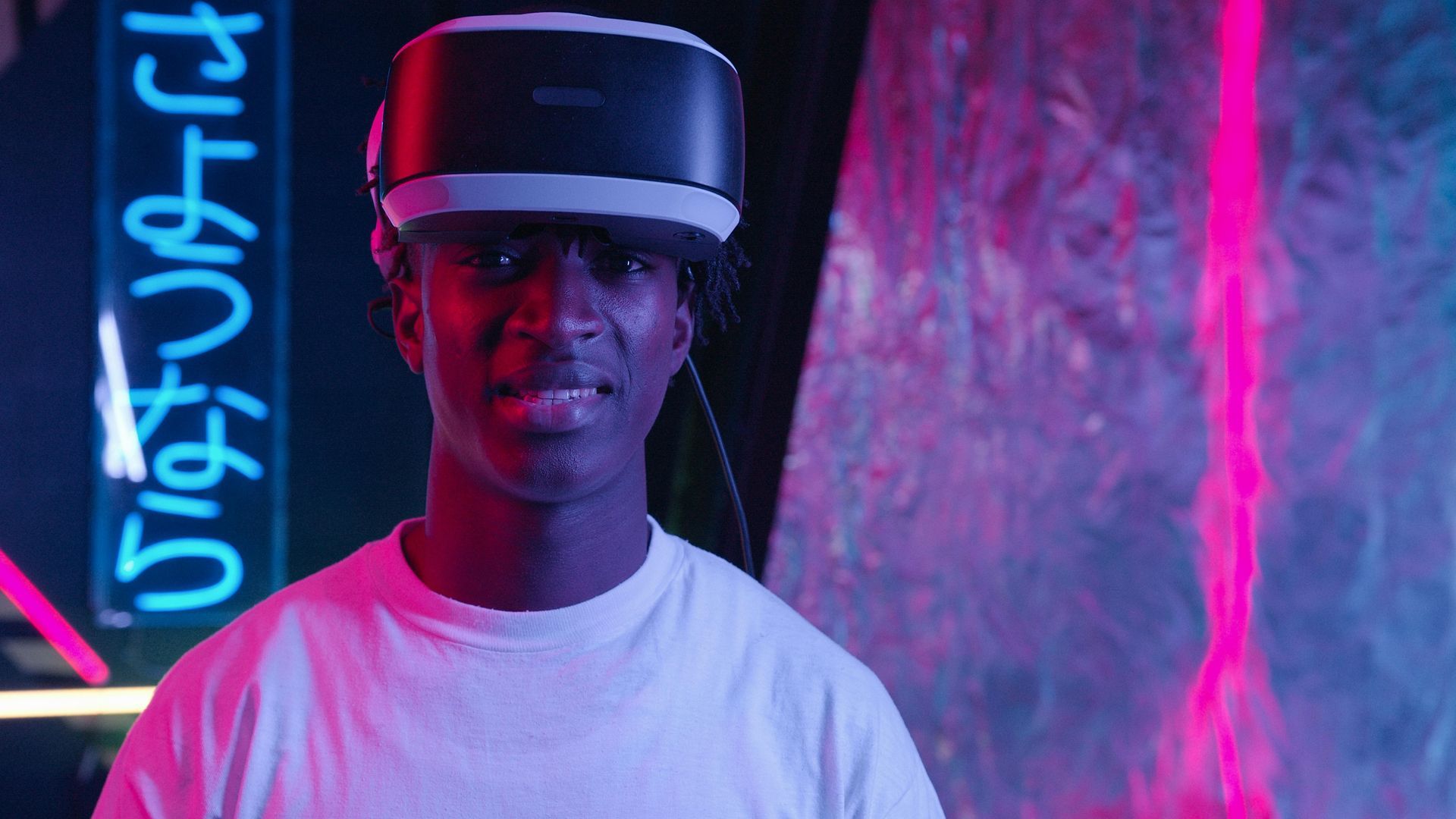 A man wearing a virtual reality headset is standing in front of a neon sign.