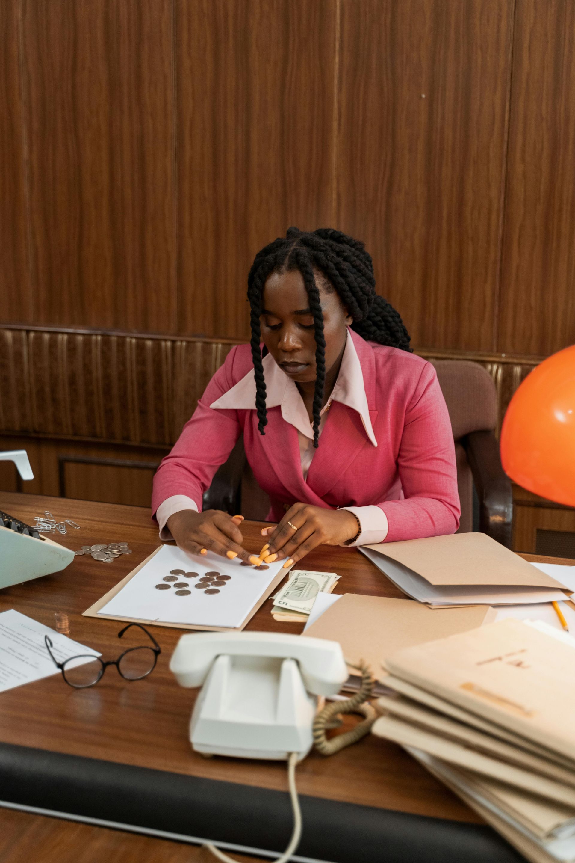 Female accountant in a pink suit counting coins and reviewing financial documents at her office desk