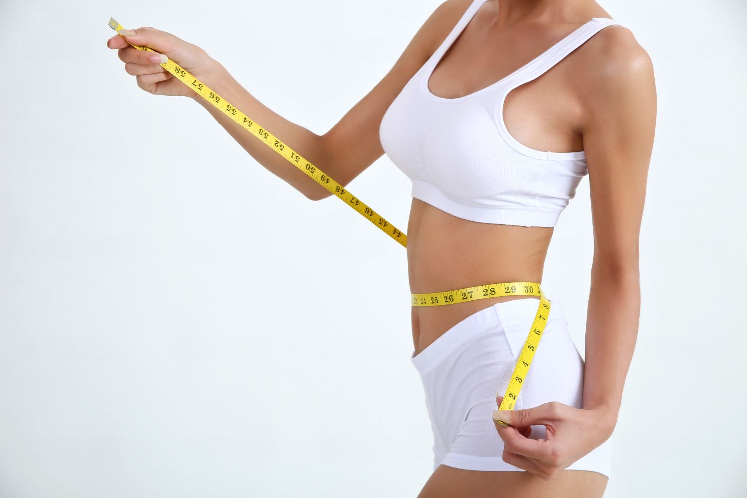 A woman is measuring her waist with a tape measure.