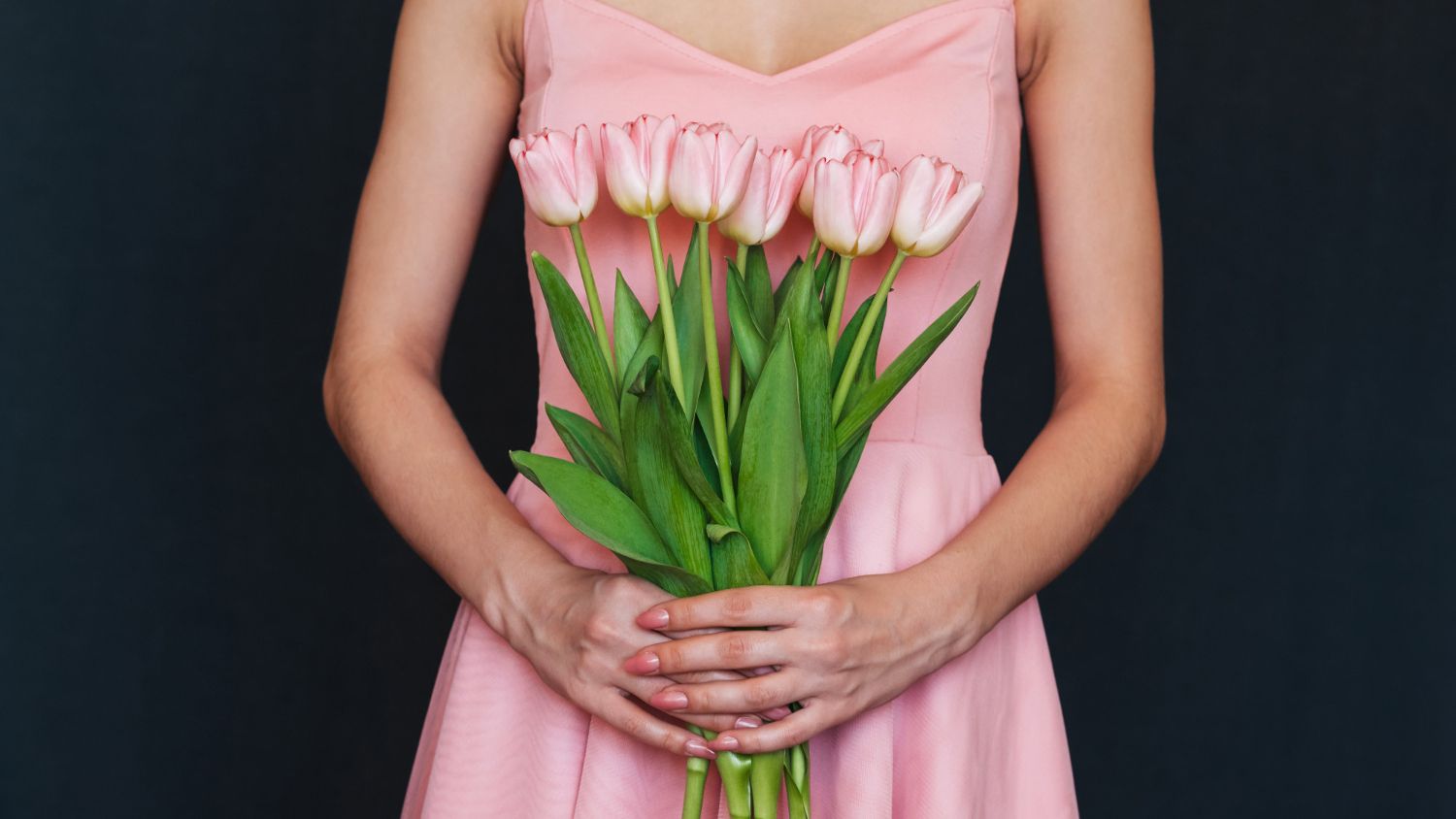A woman in a pink dress is holding a bouquet of pink tulips.