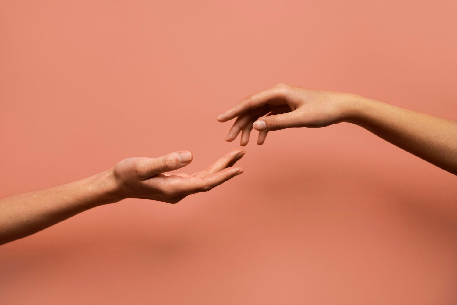 Two hands reaching towards each other, palms up, against a peach background.