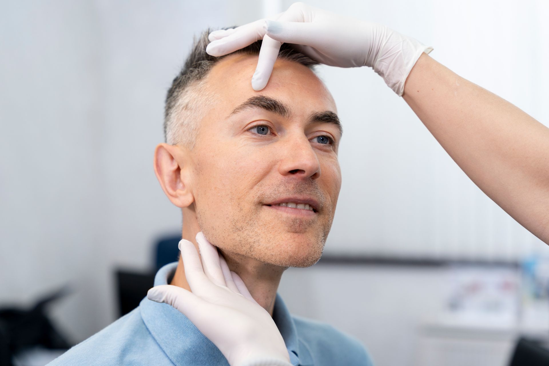 Man getting forehead and neck examined by gloved hands in a medical setting.