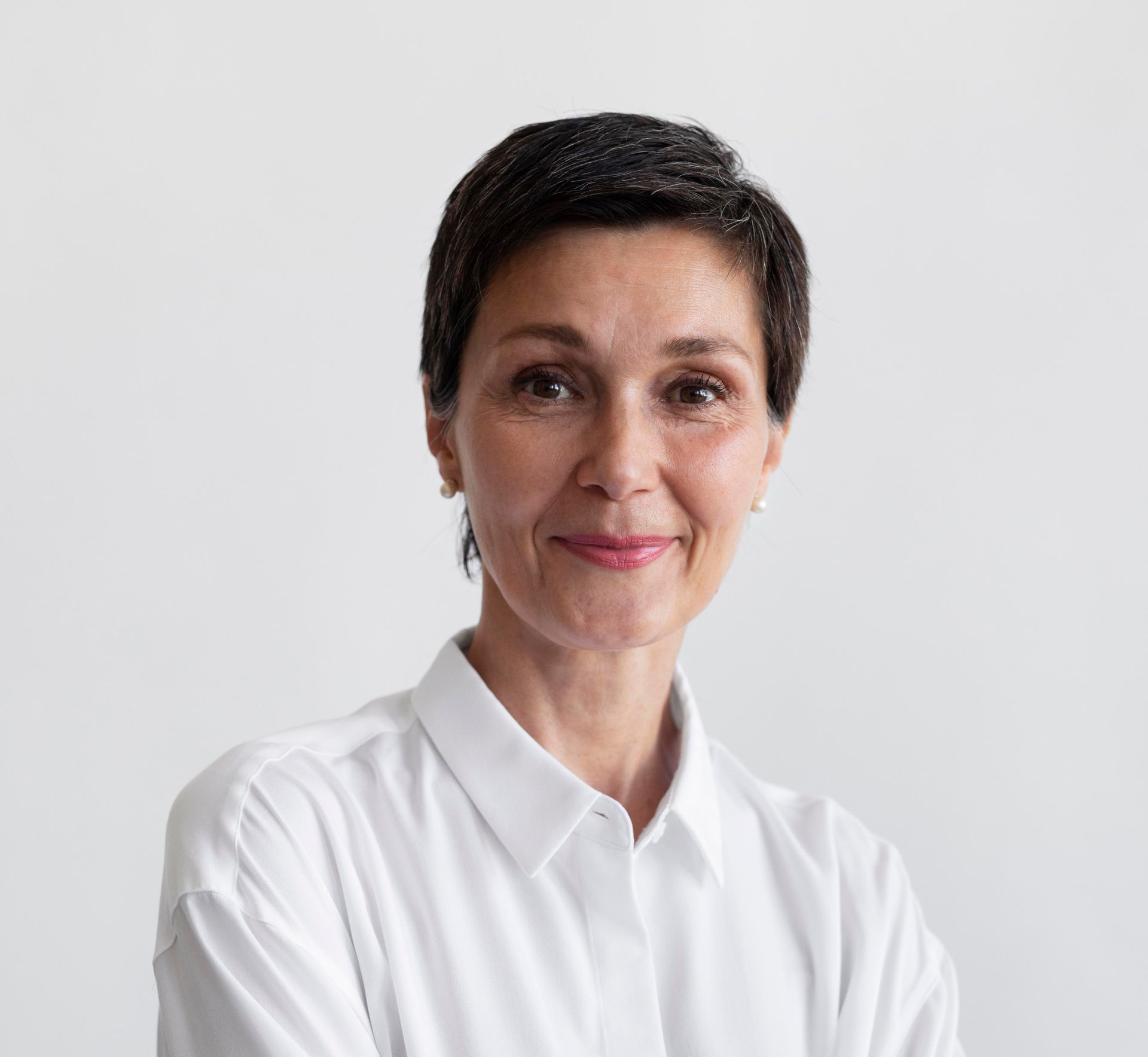 Woman with short dark hair wearing a white collared shirt, smiling.