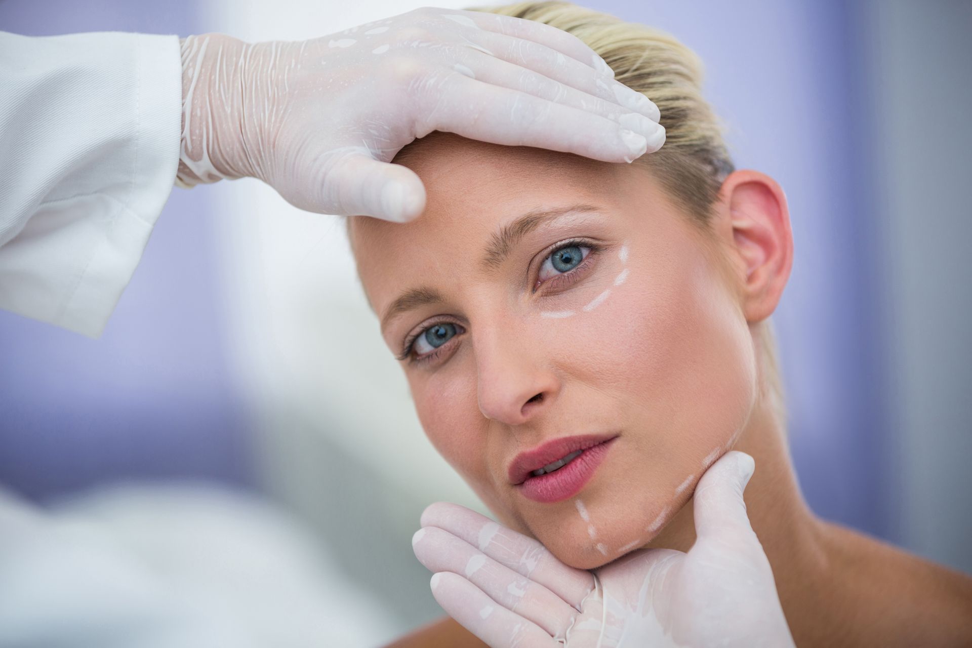 Woman with markings on face being examined by gloved hands.