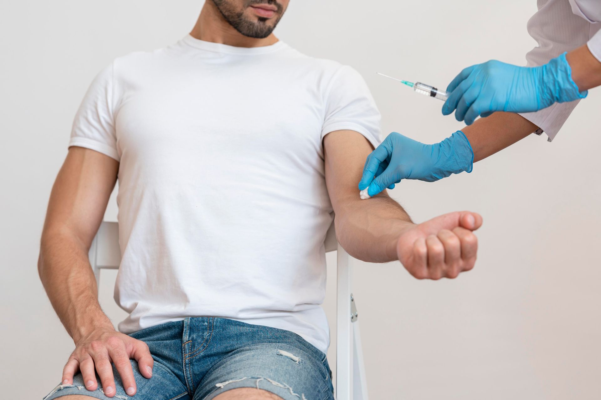 Person receiving an injection in their arm, held by someone in blue gloves, indoors.