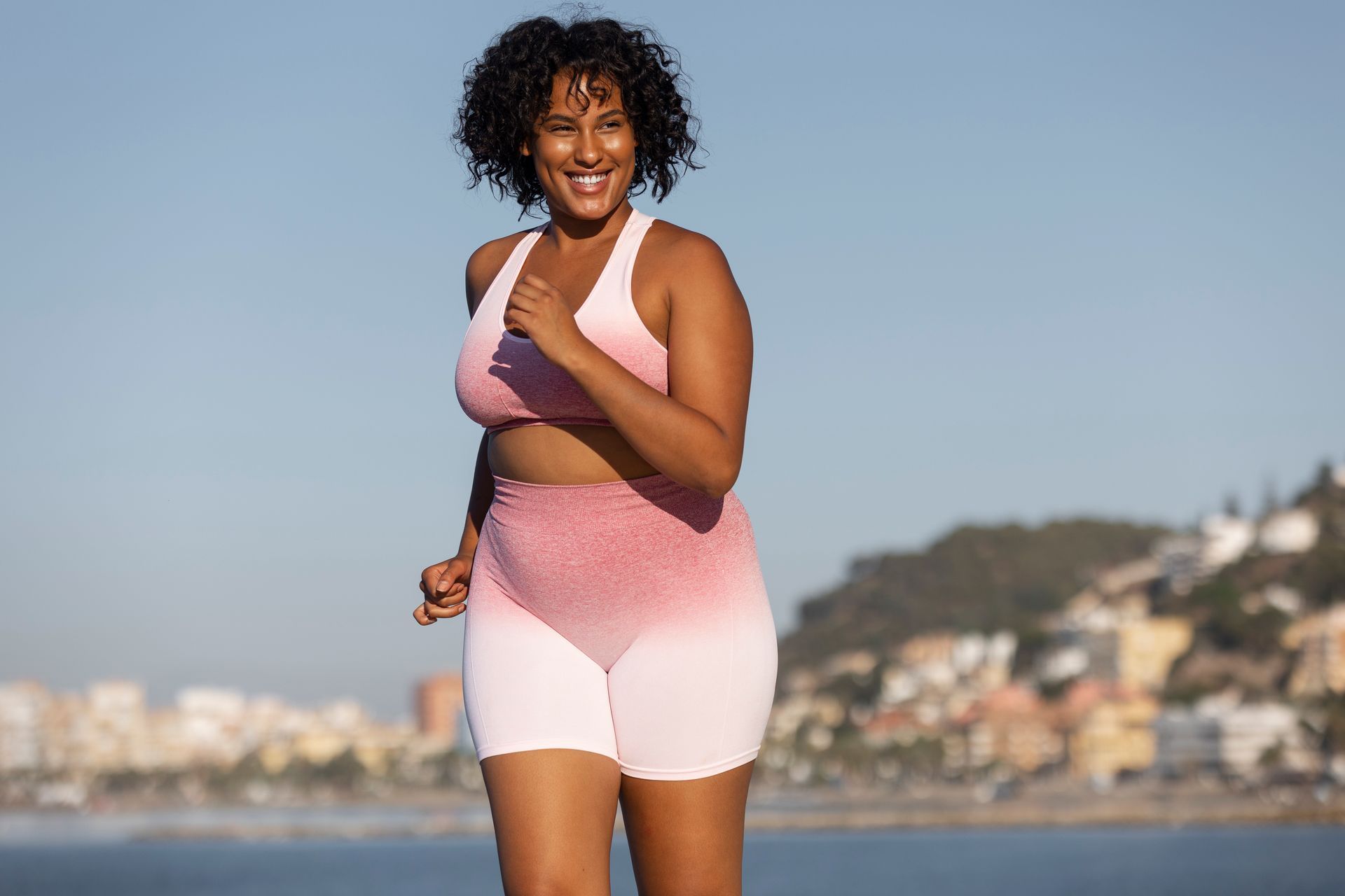Woman with long, brown, flowing hair, smiling and looking to the side against a tan background.