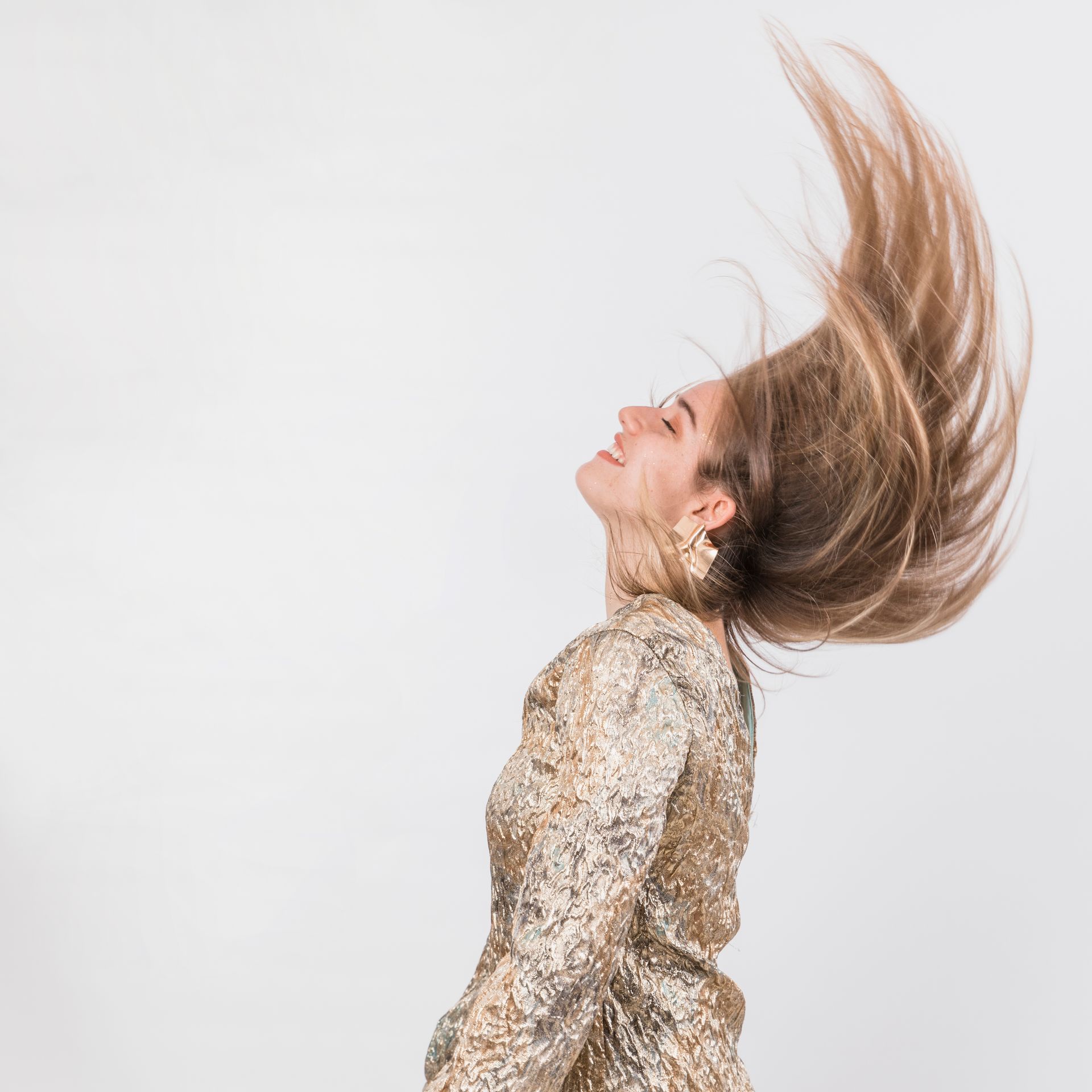 A woman in a gold dress is spinning her hair in the air.