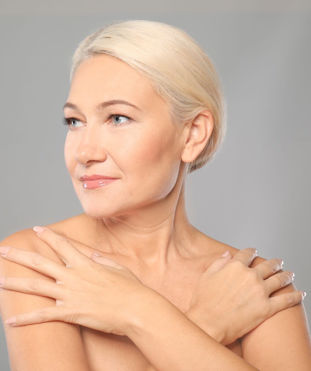 Woman with short blonde hair, looking left with arms crossed over chest. Neutral background.
