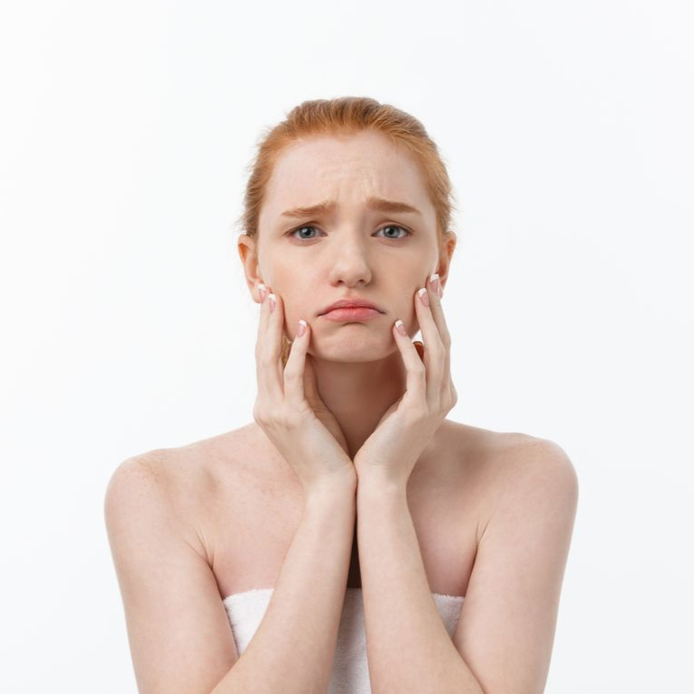 Woman with red hair, wearing a white towel, looks sad, hands on cheeks.