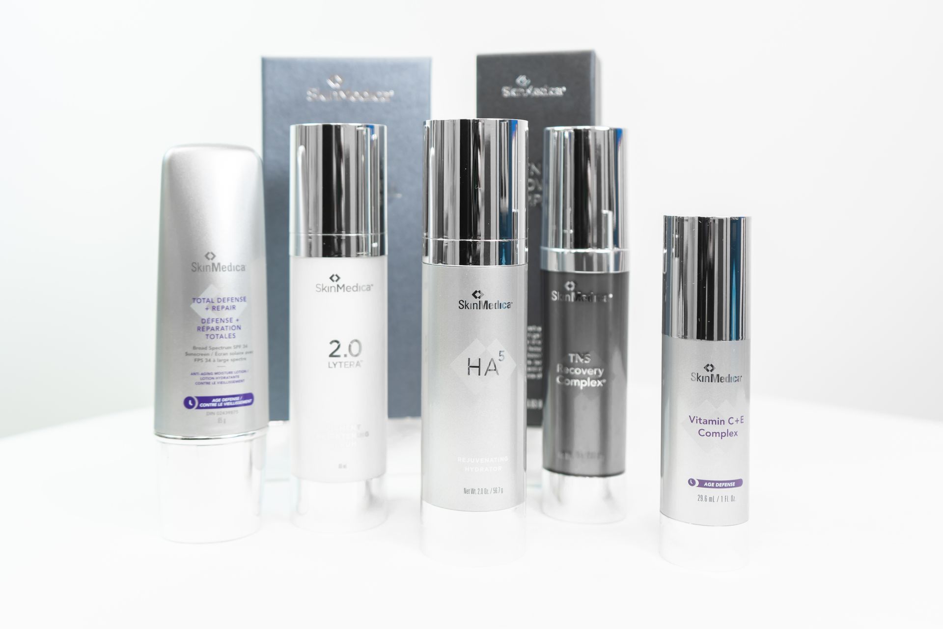 Cosmetic skincare products in various white and silver bottles, boxes on a white surface.