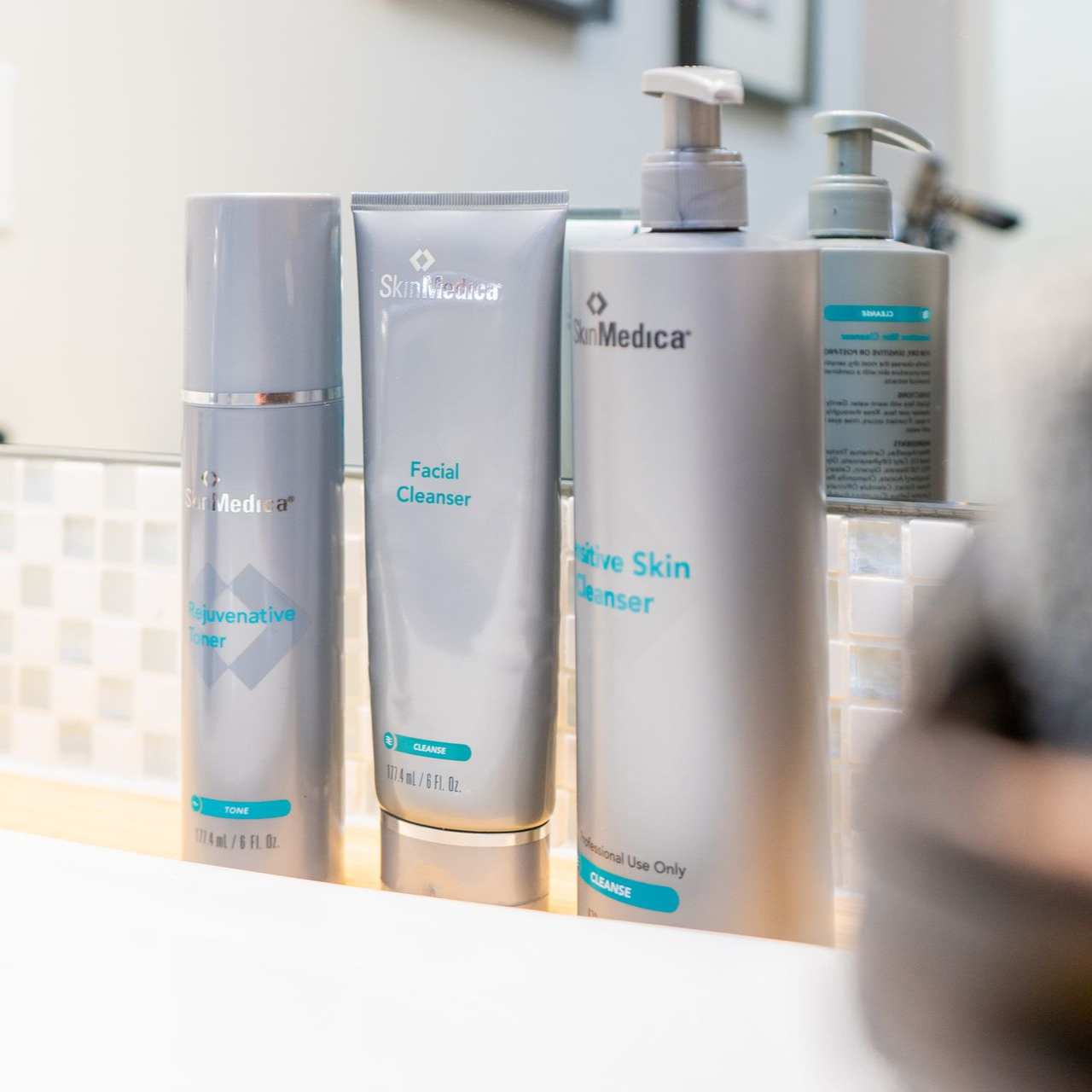 Skincare products: cleanser and toner bottles on a bathroom counter, light blue and gray colors.