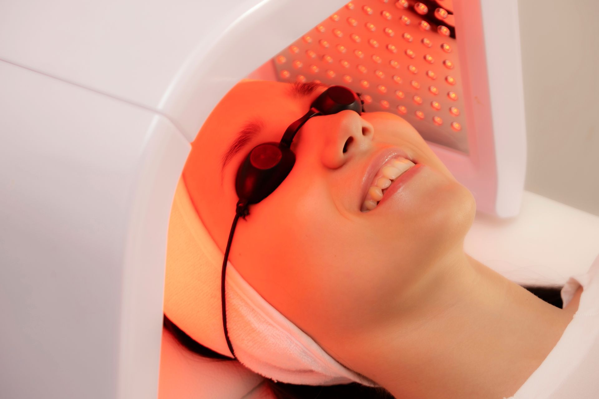Woman with eye protection smiles while receiving red light therapy.