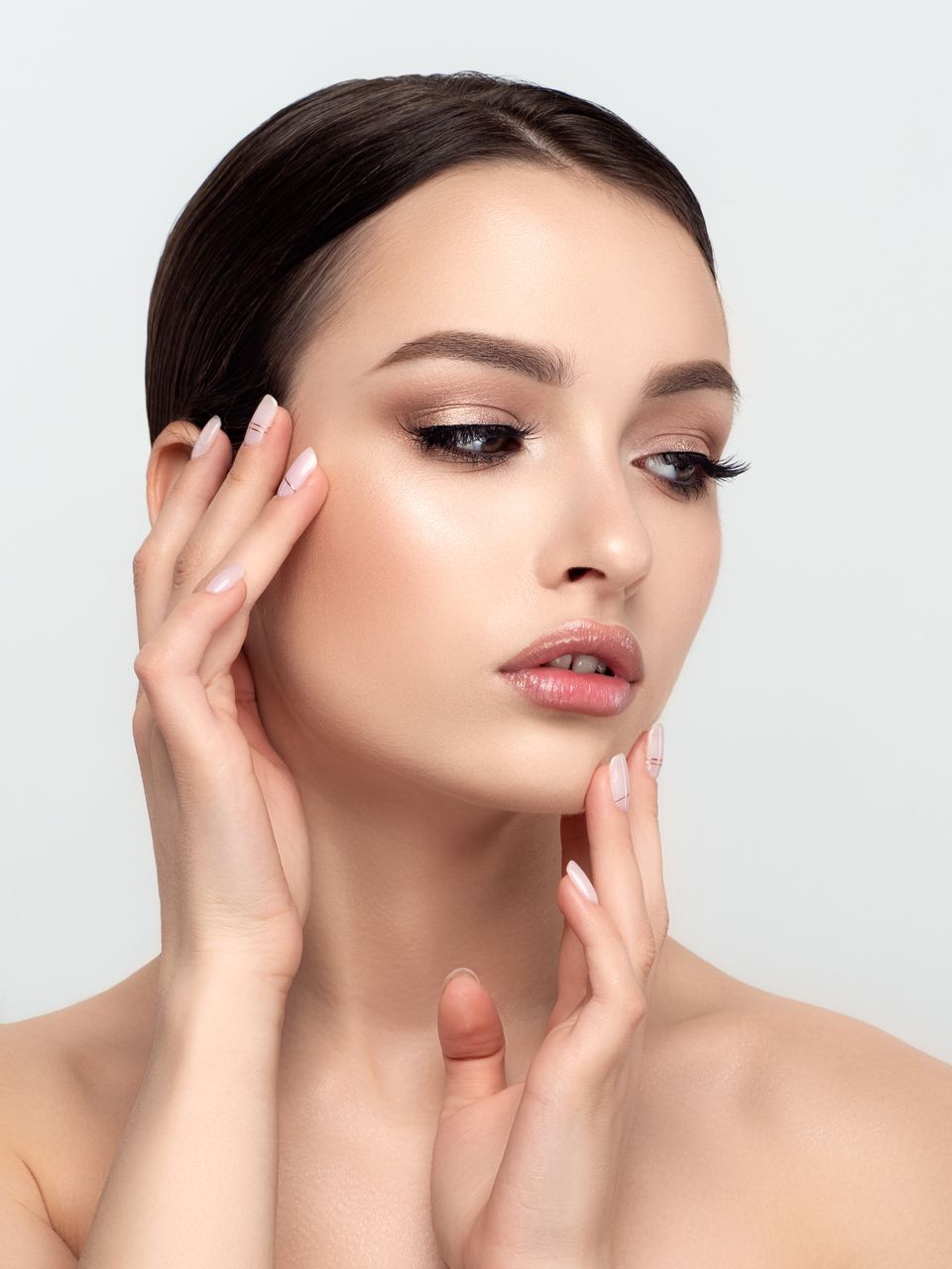 Woman with hands on face, wearing makeup, looking serene.