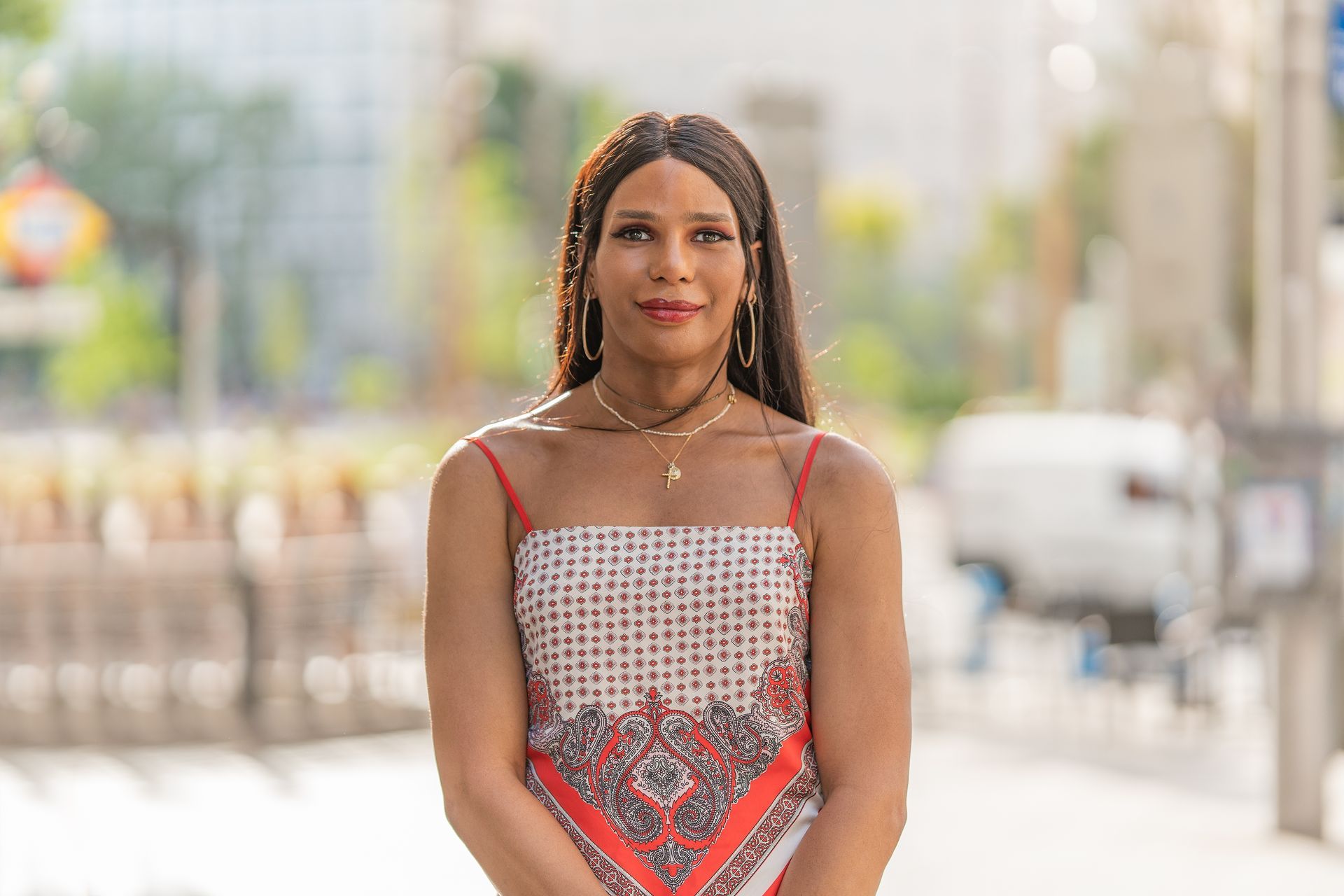 Woman in a patterned top smiles outdoors with a blurred city background.