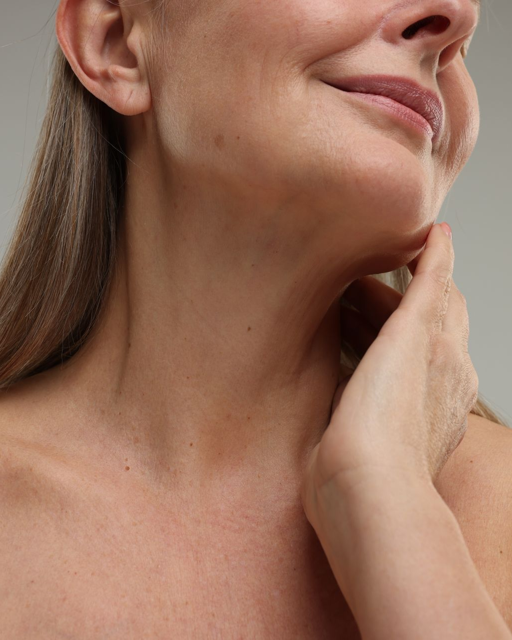 Woman's neck and face; hand gently touching her jaw. She has light skin and wrinkles.