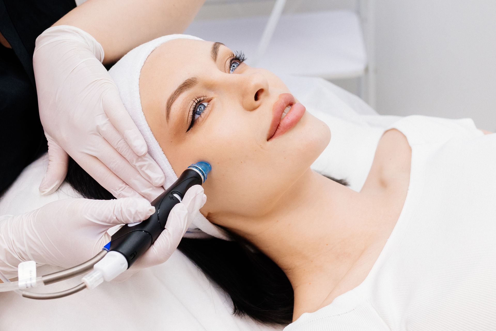 Woman receiving a facial treatment; esthetician's gloved hands holding device on face.