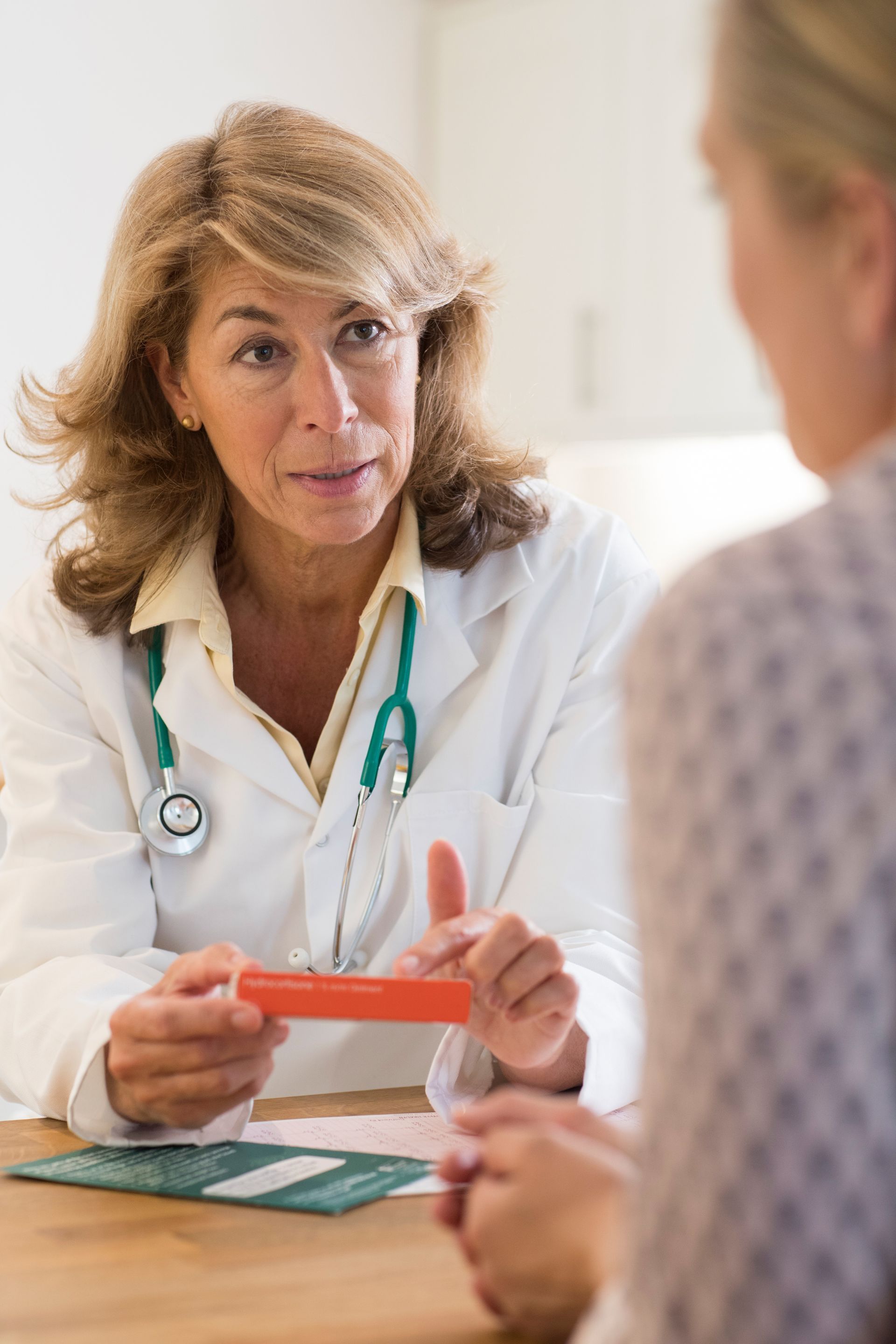 Doctor discussing a prescription with a patient across a desk, holding a red card.