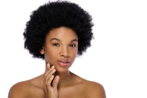 a woman with an afro is touching her face and looking at the camera .