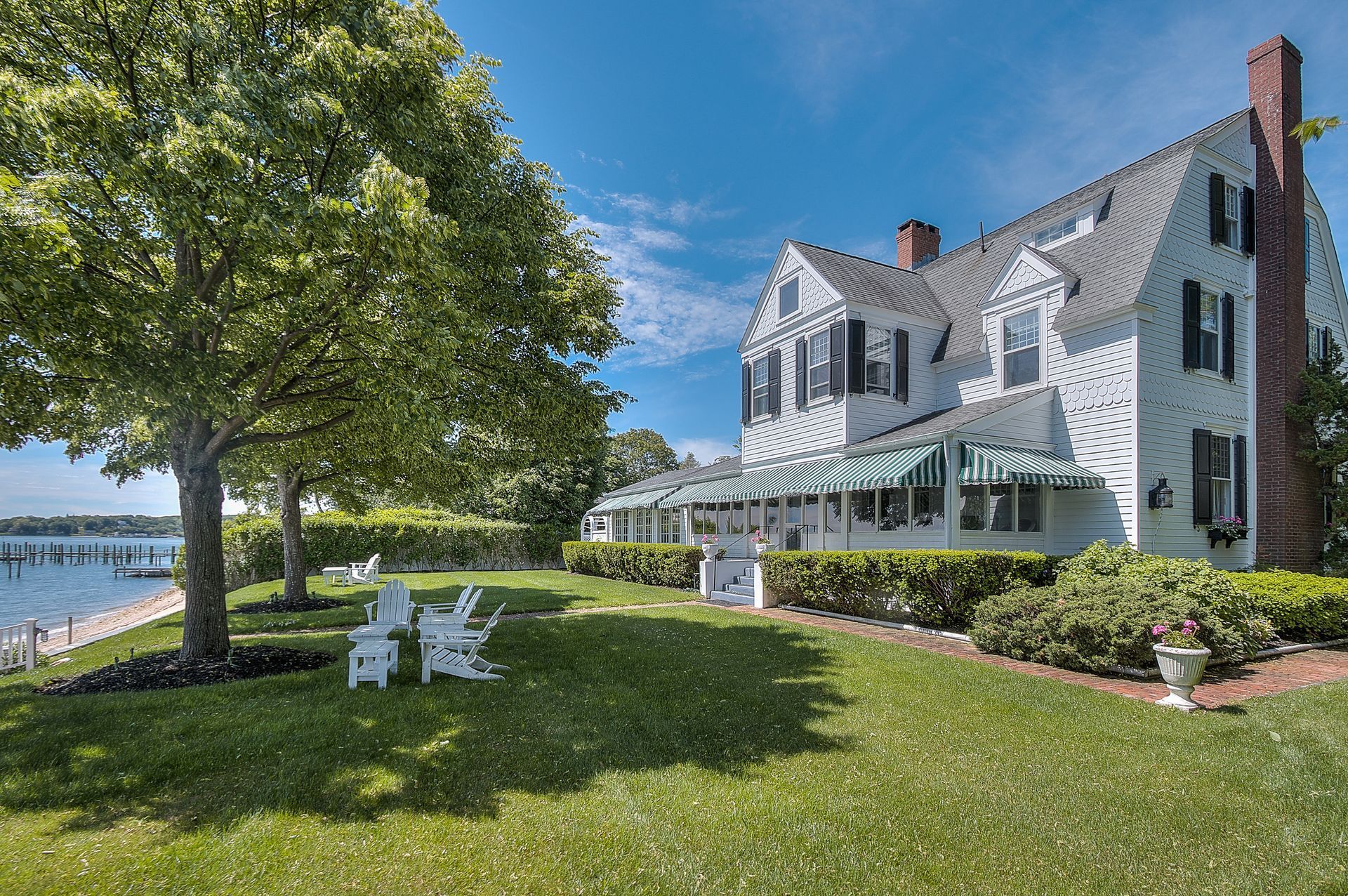 A large white house is sitting on top of a lush green lawn next to a body of water.