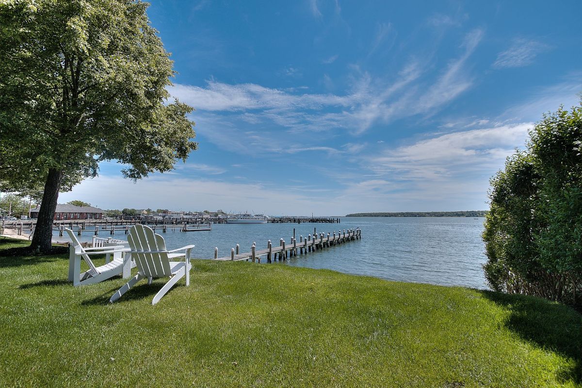 Two white chairs are sitting on a lush green lawn next to a body of water.