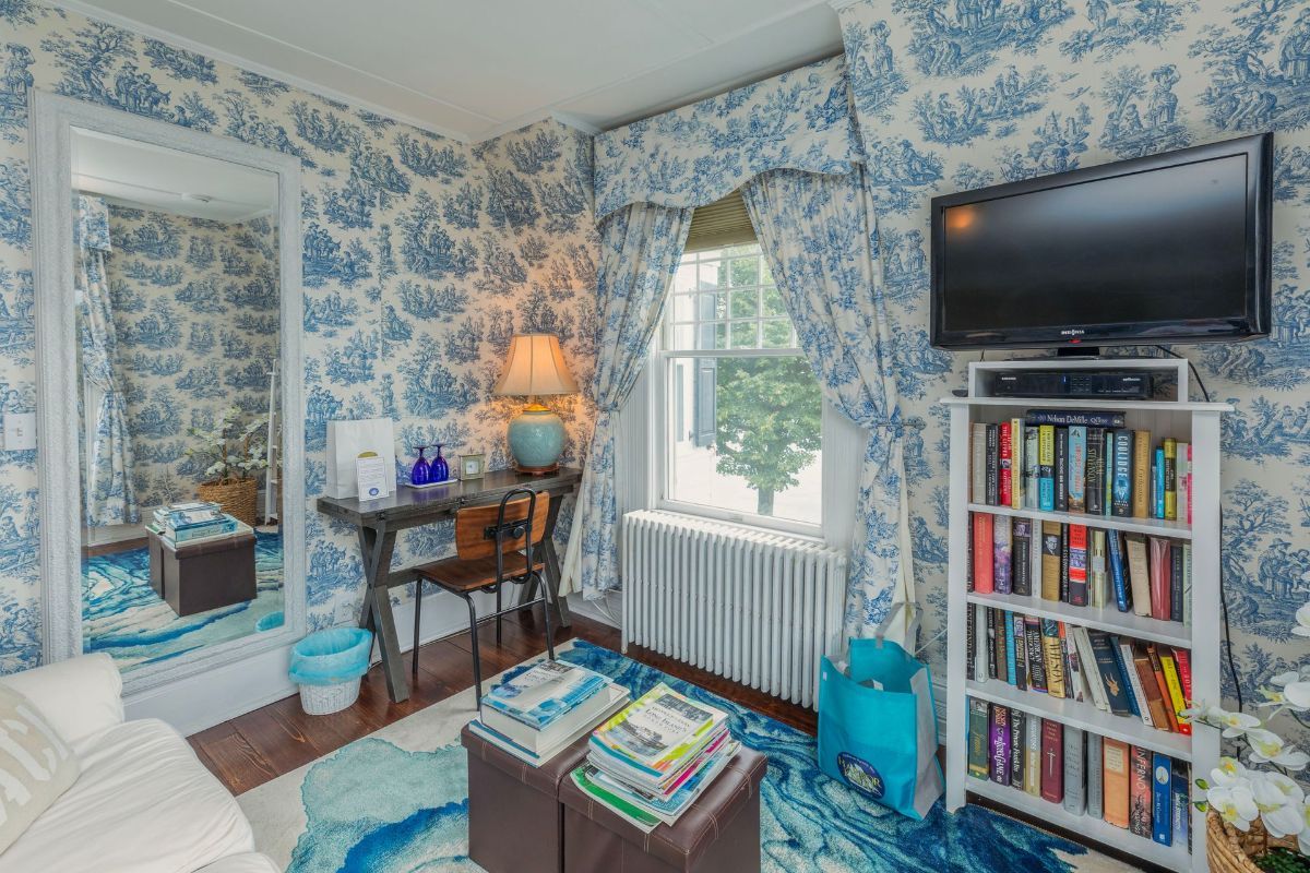 A living room with blue and white toile de jouy wallpaper and a flat screen tv.