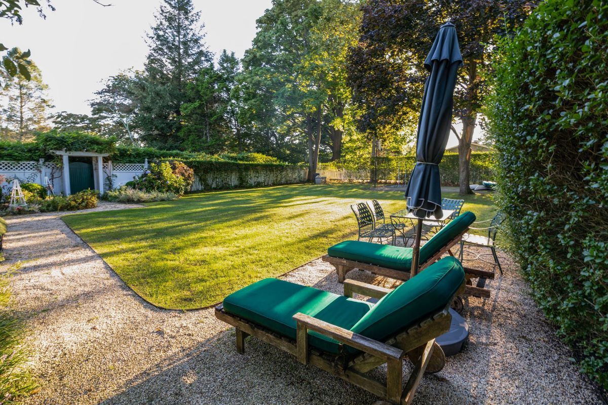 There are two lounge chairs and an umbrella in the backyard.