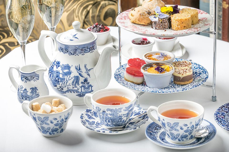 A table topped with cups of tea , a teapot , and a variety of desserts.