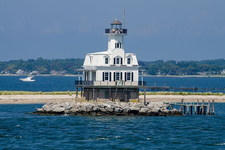 White lighthouse on a rocky islet surrounded by blue water under a clear sky