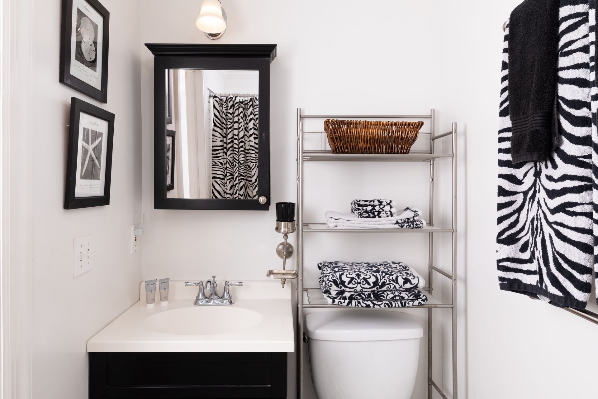 A bathroom with a toilet , sink , mirror and zebra print towels.