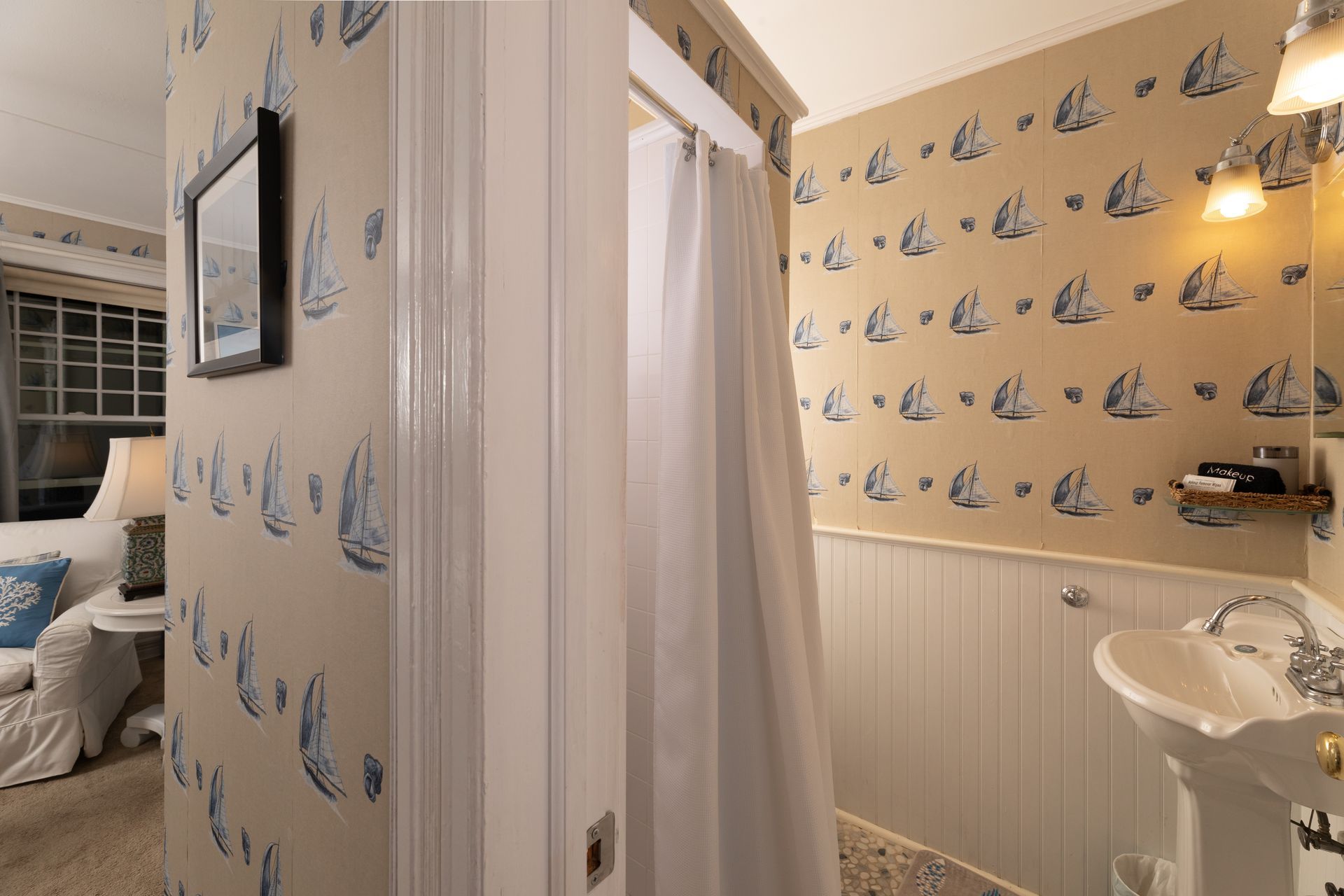 A bathroom with a sink and a shower with sailboats on the wall