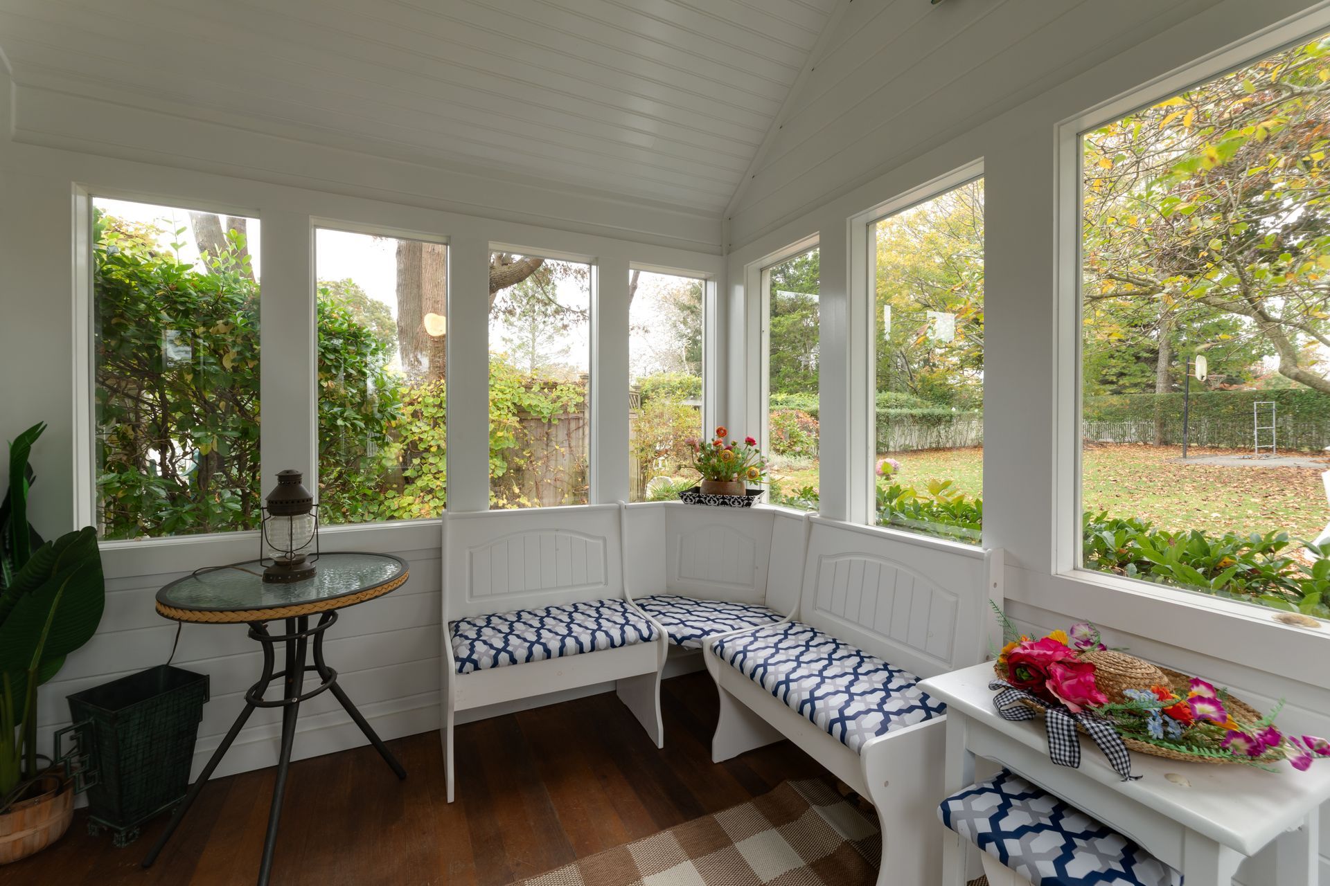A sun room with a bench , table and windows.