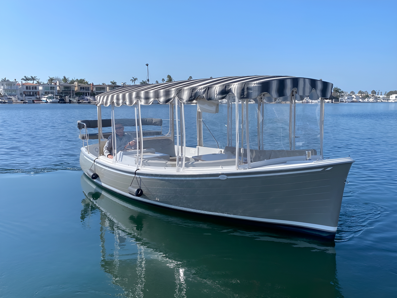 White boat with canopy floating on calm blue water near a coastal town