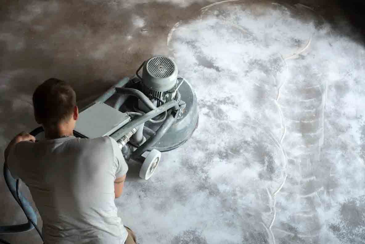 Person using a floor sander on a dusty floor, creating a cloud of dust.