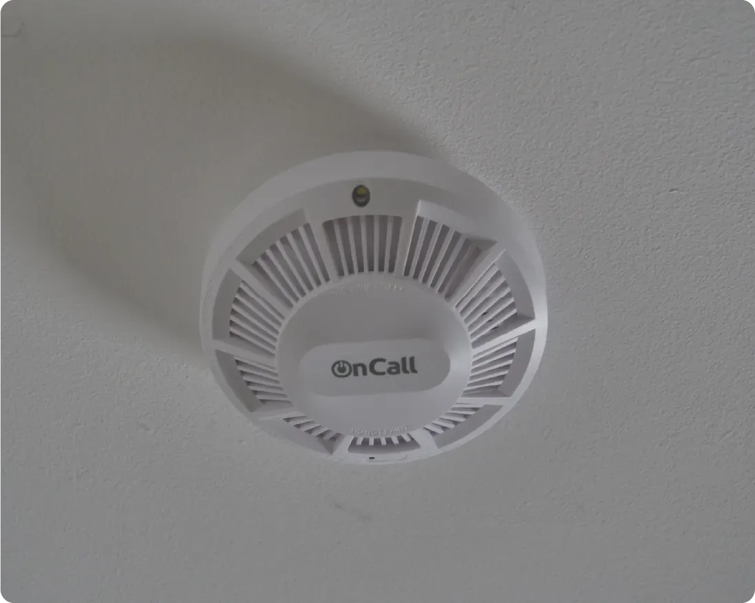 White smoke detector mounted on a white ceiling;