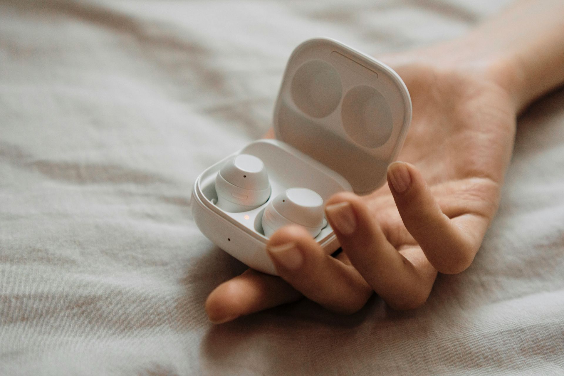 A person is holding a pair of white earbuds in their hand.