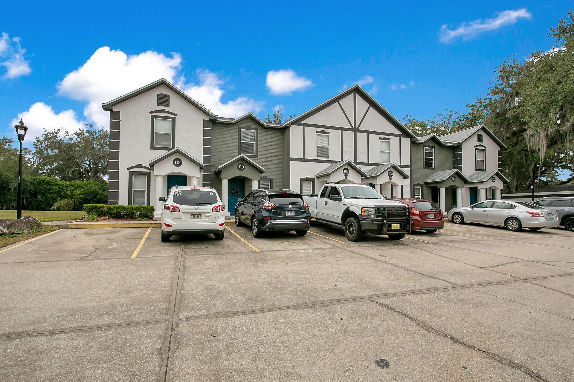 A row of cars are parked in front of a large apartment building.