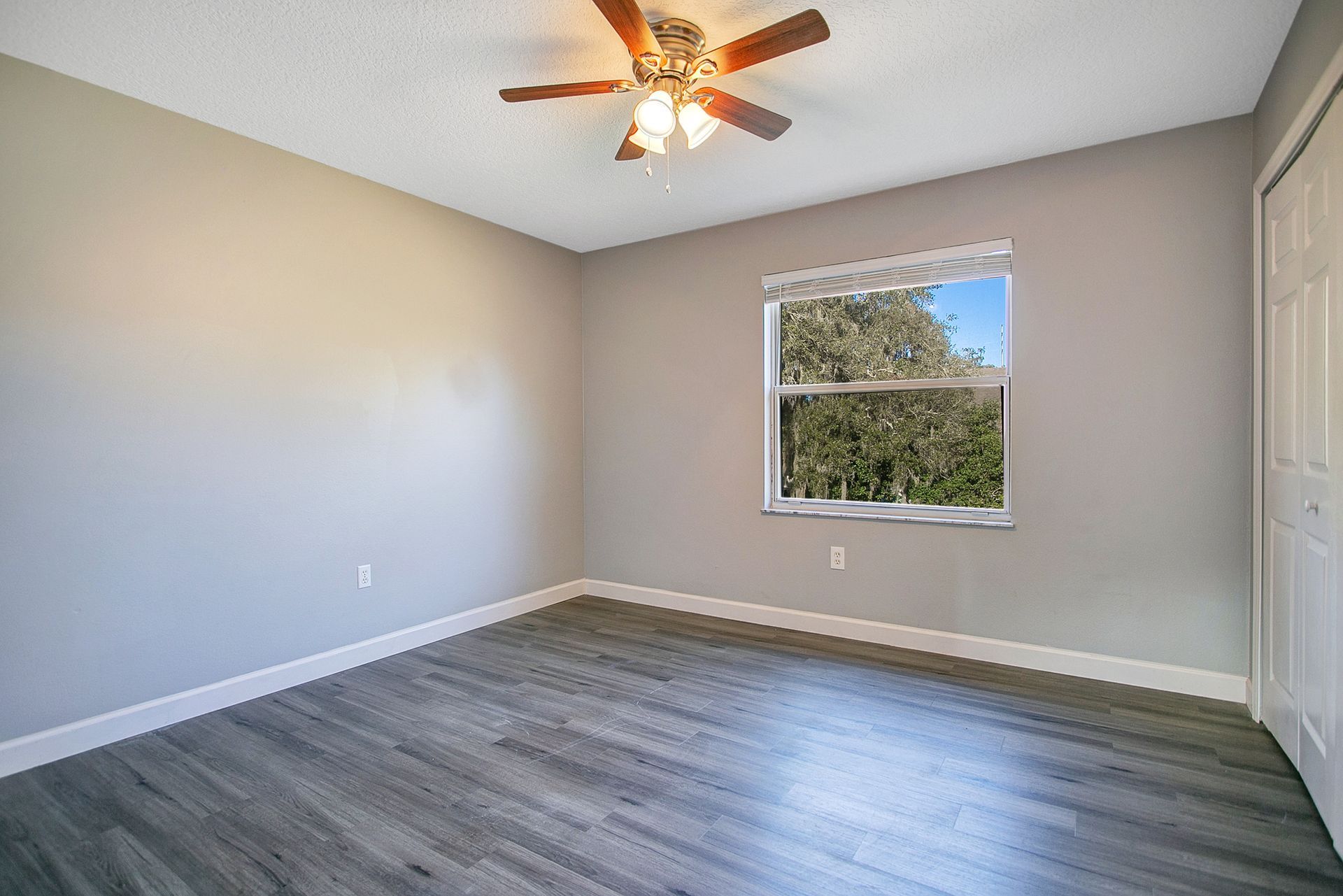 An empty bedroom with a ceiling fan and a window.