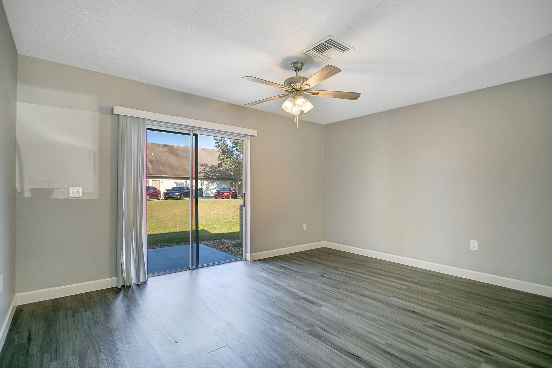 An empty living room with a ceiling fan and sliding glass doors.
